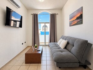 En moderne stue med en grå sofa, et sofabord, et fladskærms-tv og et maleri af en solnedgang.