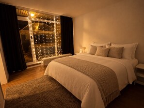 A bedroom with a large bed, a radiator, a nightstand, and a window with curtains.