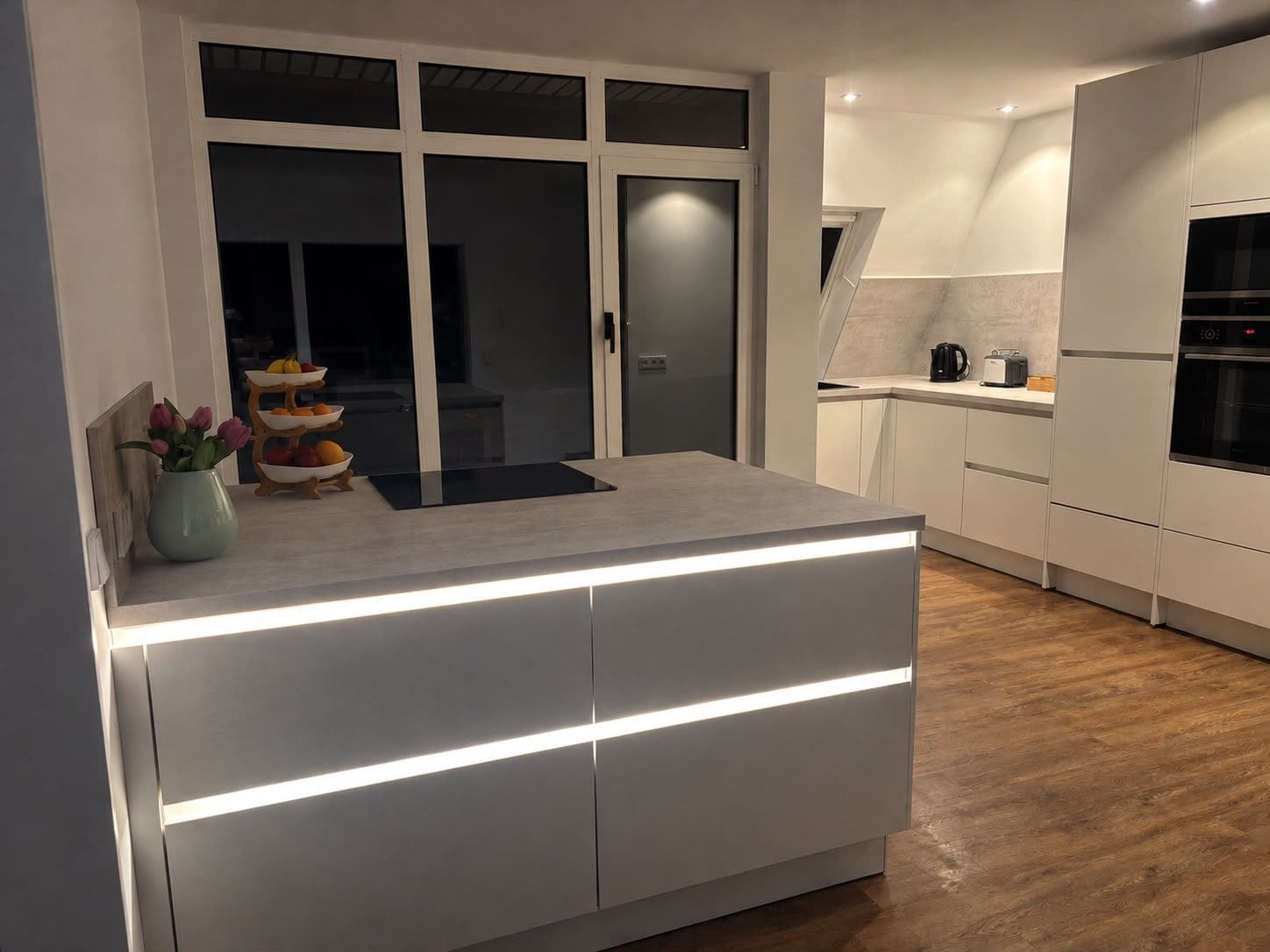 A modern kitchen with a central island, white cabinetry, and a built-in oven.