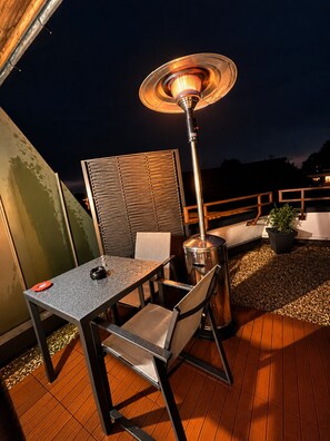 An outdoor patio area with a table and chairs, a floor heater, and a potted plant.