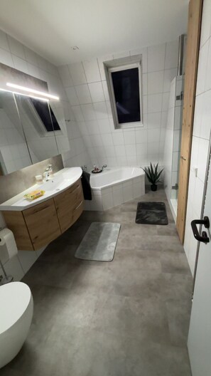 A modern bathroom with a large sink, a bathtub, and a small window.