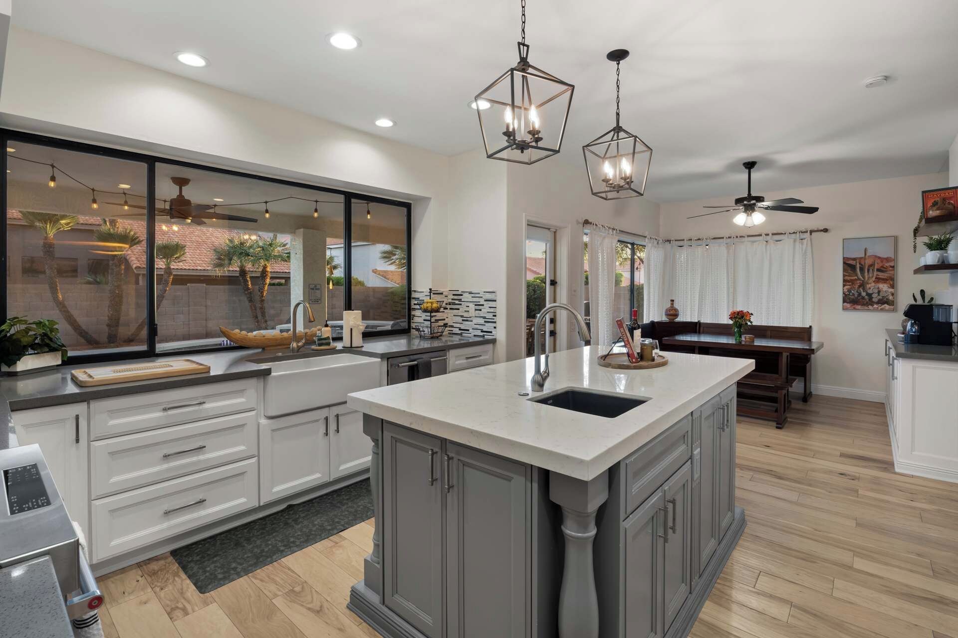 A modern kitchen with a large island, pendant lighting, and a view of the outdoors.