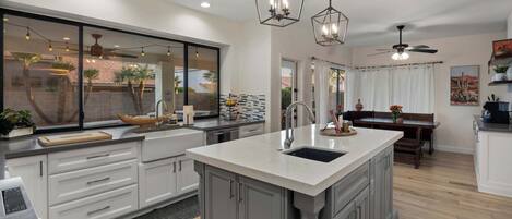 A modern kitchen with a large island, pendant lighting, and a view of the outdoors.