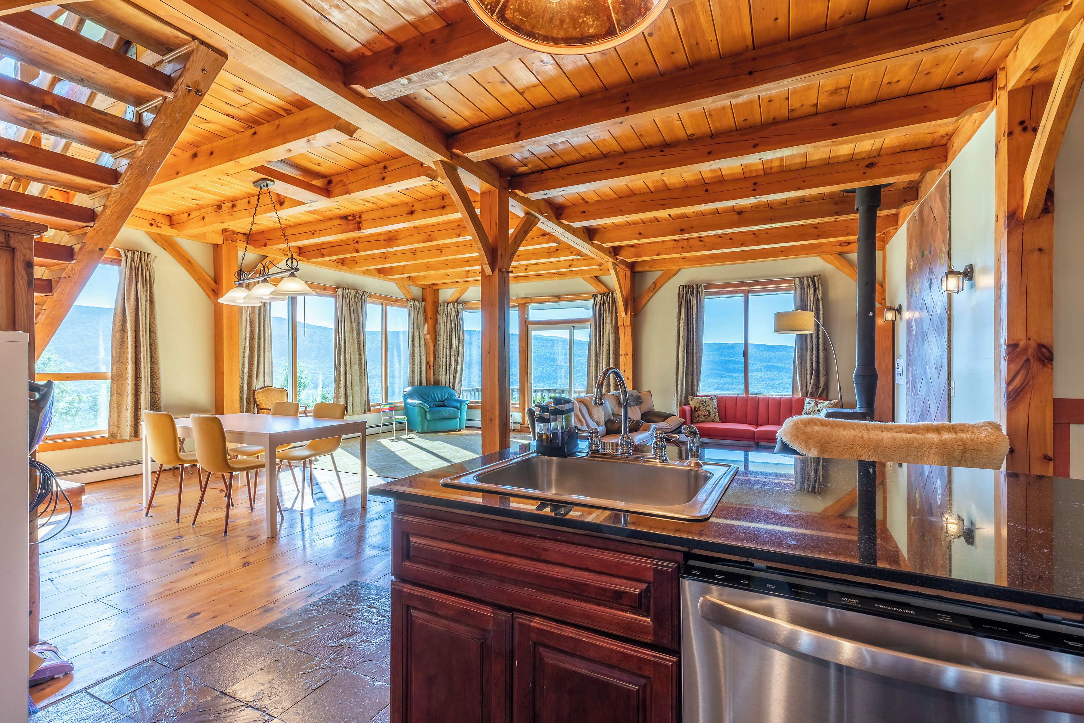 Une cuisine spacieuse avec des poutres en bois, un grand îlot central doté d’un évier, et un coin repas avec des chaises et une table.