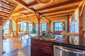 A spacious kitchen with wooden beams, a large island with a sink, and a dining area with chairs and a table.
