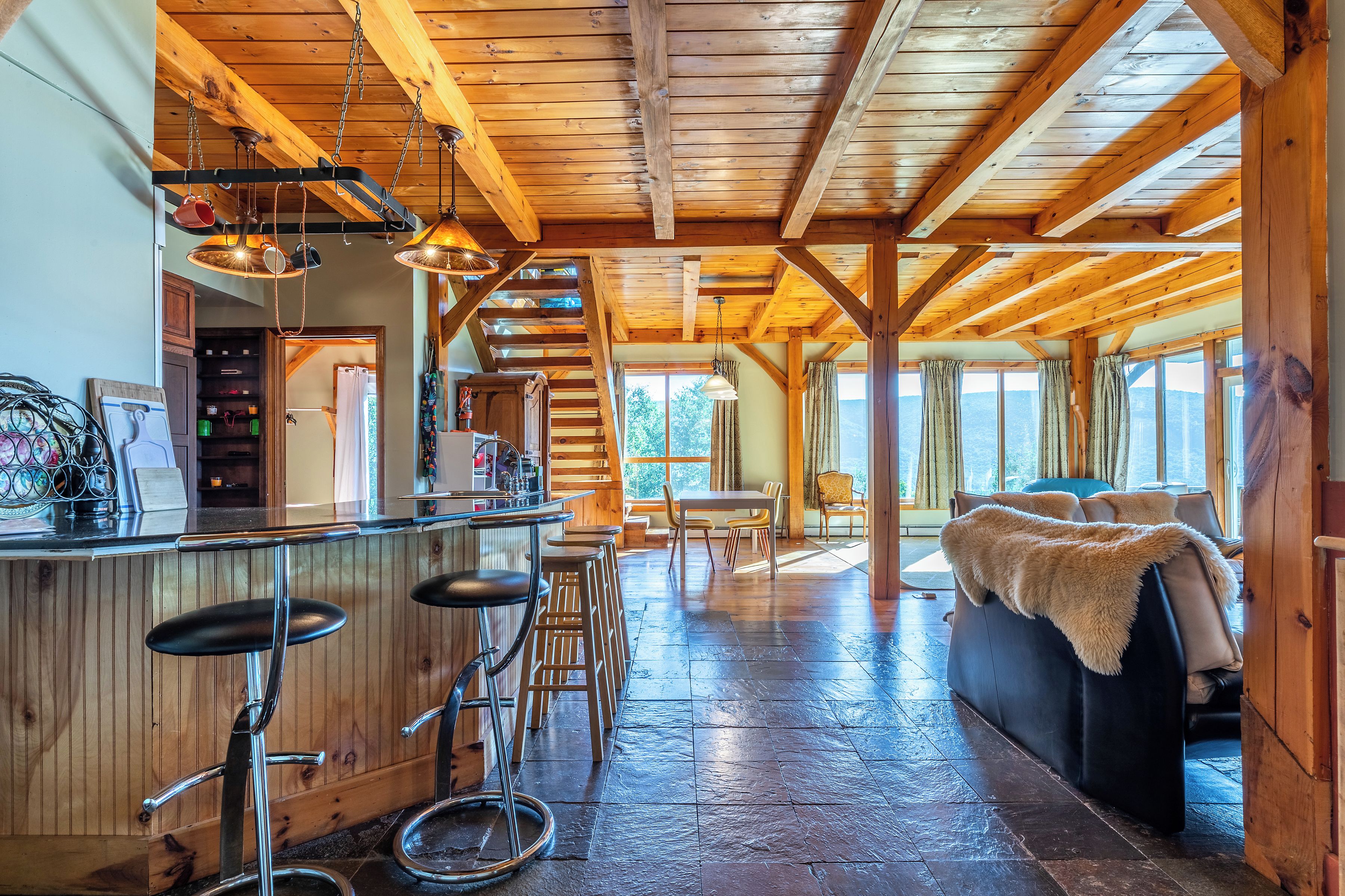 A rustic interior with a wooden ceiling, a bar area with stools, a sofa, and a dining table.