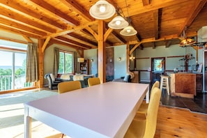 A spacious dining area with a long table and chairs, wooden beams on the ceiling, and a view of the outdoors.