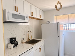 A kitchen with white cabinets, a built-in microwave, a stainless steel sink, and a white refrigerator. - Updated 2BR Cincinnati Apartment for Extended Stays - Unit 1 (Cincinnati)
