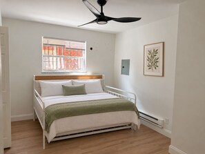 A bedroom with a bed, a window, a ceiling fan, and a wall-mounted light fixture. - Updated 2BR Cincinnati Apartment for Extended Stays - Unit 1 (Cincinnati)