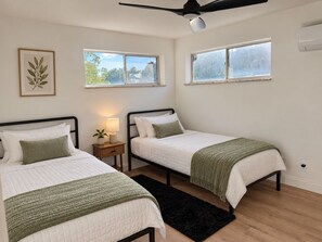 A bedroom with two beds, a ceiling fan, a window, and a plant on a bedside table. - Updated 2BR Cincinnati Apartment for Extended Stays - Unit 1 (Cincinnati)