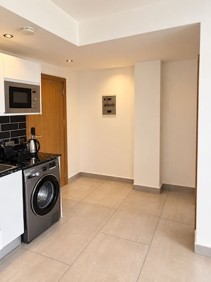 A compact kitchen with a microwave, stove, and washing machine. - Sky Suites Quattro (Accra)