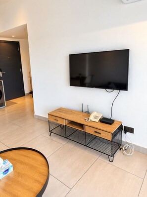 A modern hotel room with a flat-screen TV mounted on the wall, a wooden desk with drawers, a telephone, and a power outlet. - Sky Suites Quattro (Accra)