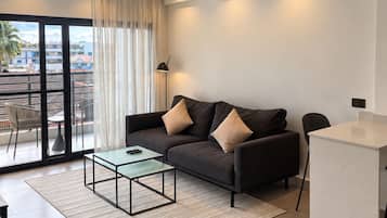 Ein modernes Wohnzimmer mit einer Couch, einem Glastisch und Blick durch ein großes Fenster.