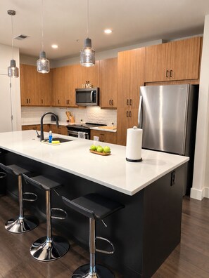 Una cucina moderna con mobili in legno, elettrodomestici in acciaio inossidabile, un'isola centrale con sgabelli da bar e illuminazione a sospensione.
