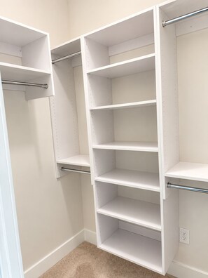 Armadio a muro con scaffali multipli e aste appendiabiti, una presa di corrente a destra e un tappeto beige.