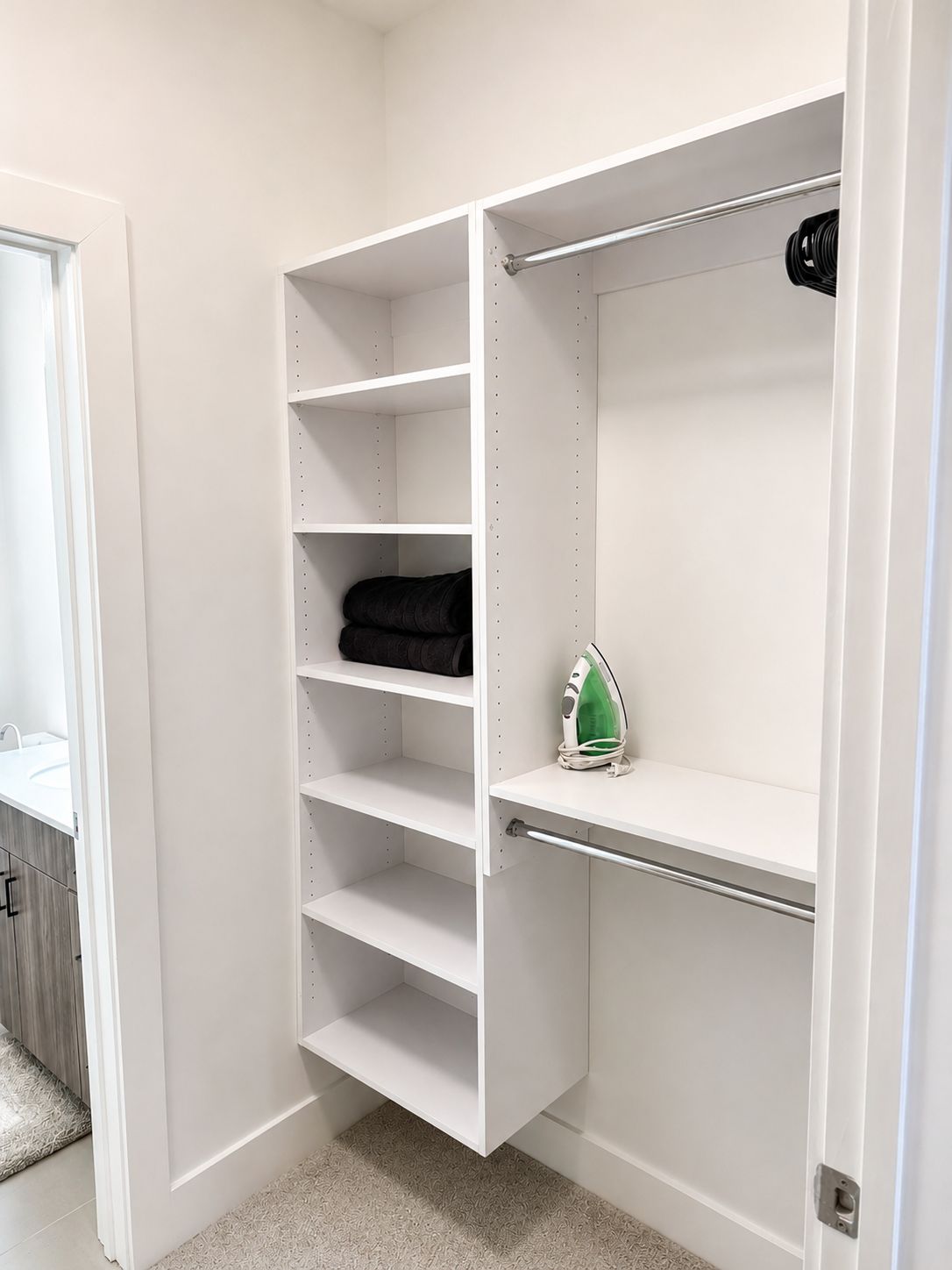Un armario blanco con estantes abiertos, una barra para colgar ropa y una puerta con picaporte.