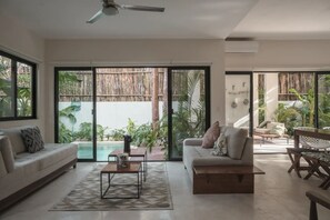Un vaste espace de vie doté d’une grande porte-fenêtre coulissante donnant accès à une piscine, d’un ventilateur de plafond et d’un canapé moderne.