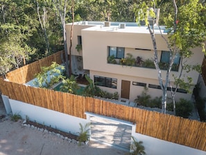 Un bâtiment moderne à deux étages, doté d’un toit plat, entouré d’une clôture en bois et d’une végétation luxuriante.