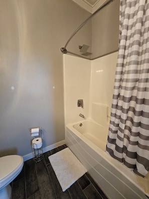 Et badeværelse med toilet, bruser og badekar.