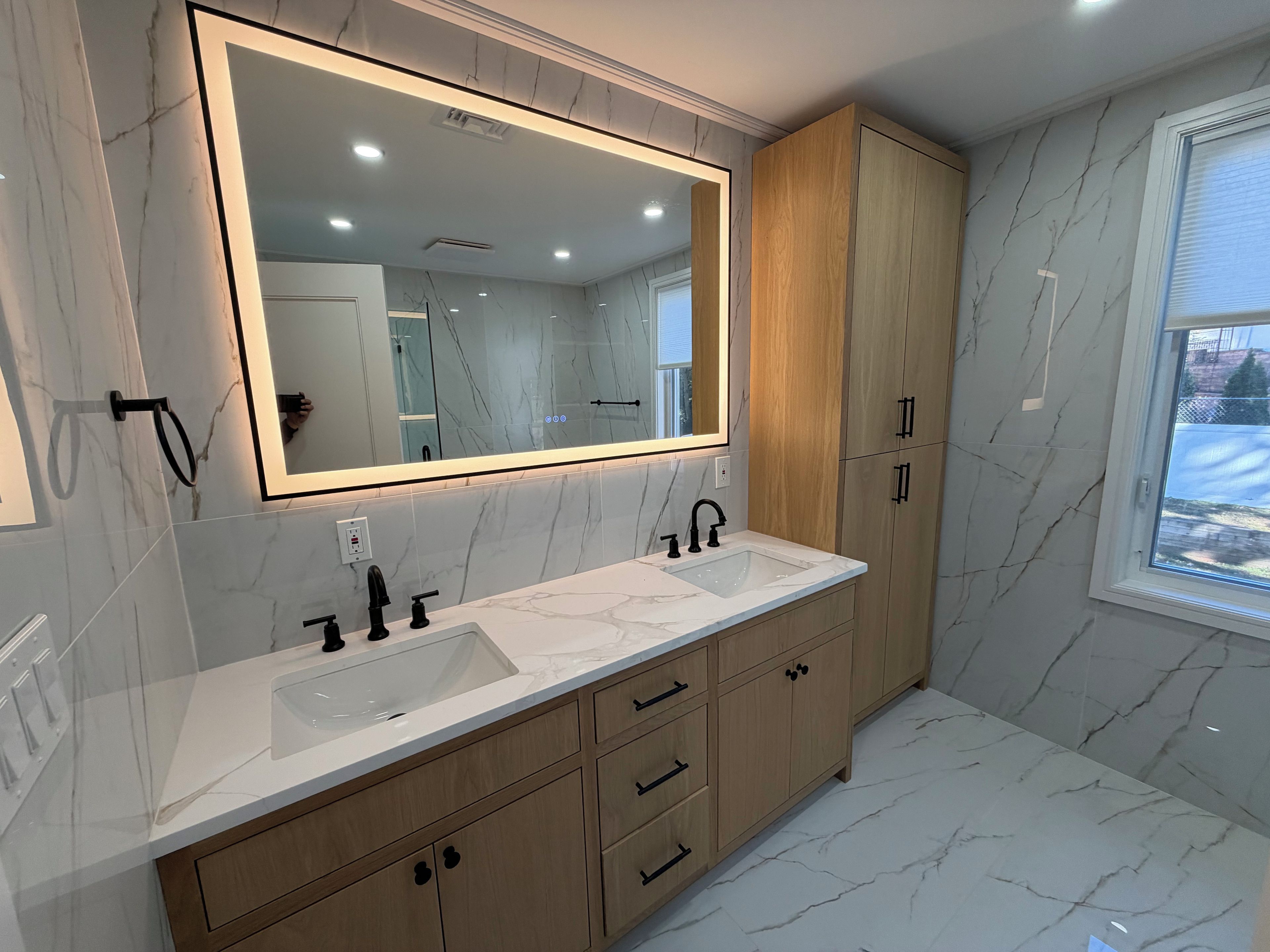 Un baño moderno con un espejo grande, dos lavamanos, armarios de madera y una ventana.