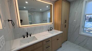 Un baño moderno con un espejo grande, dos lavamanos, armarios de madera y una ventana.