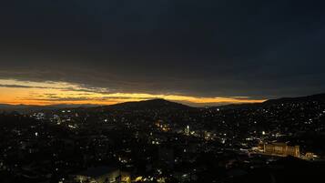 Paisagem urbana ao anoitecer, com edifícios iluminados e uma cordilheira ao fundo.