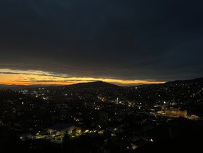 Eine städtische Szene im Abendlicht, mit beleuchteten Gebäuden und einer Bergkette im Hintergrund.