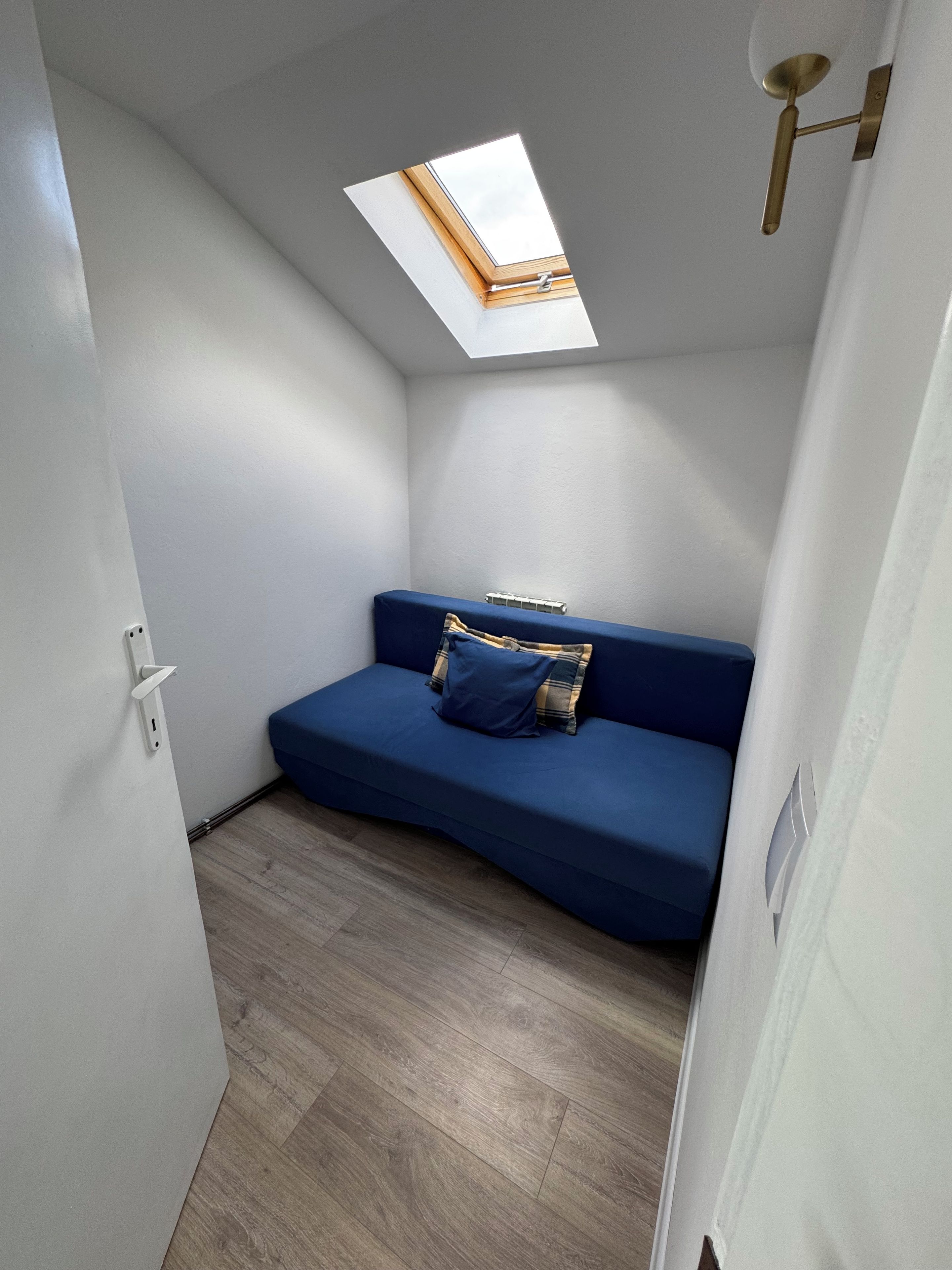 A small, narrow room with a skylight, a blue sofa, and a radiator.