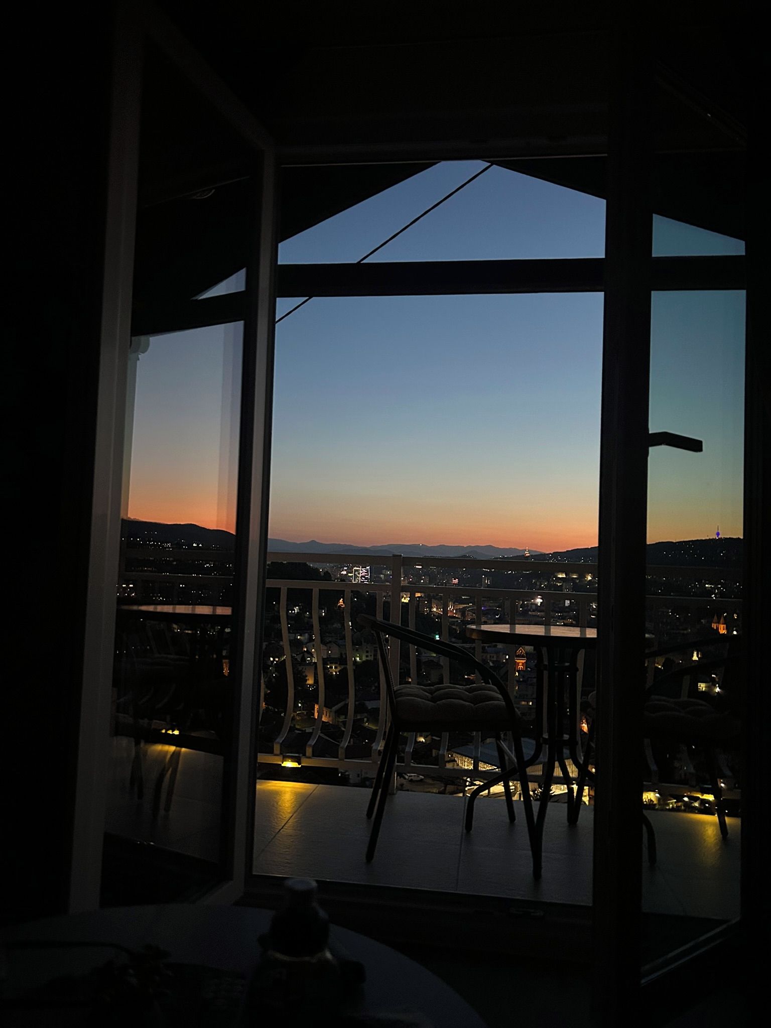 Quarto com uma grande janela com vista para a paisagem urbana ao entardecer.