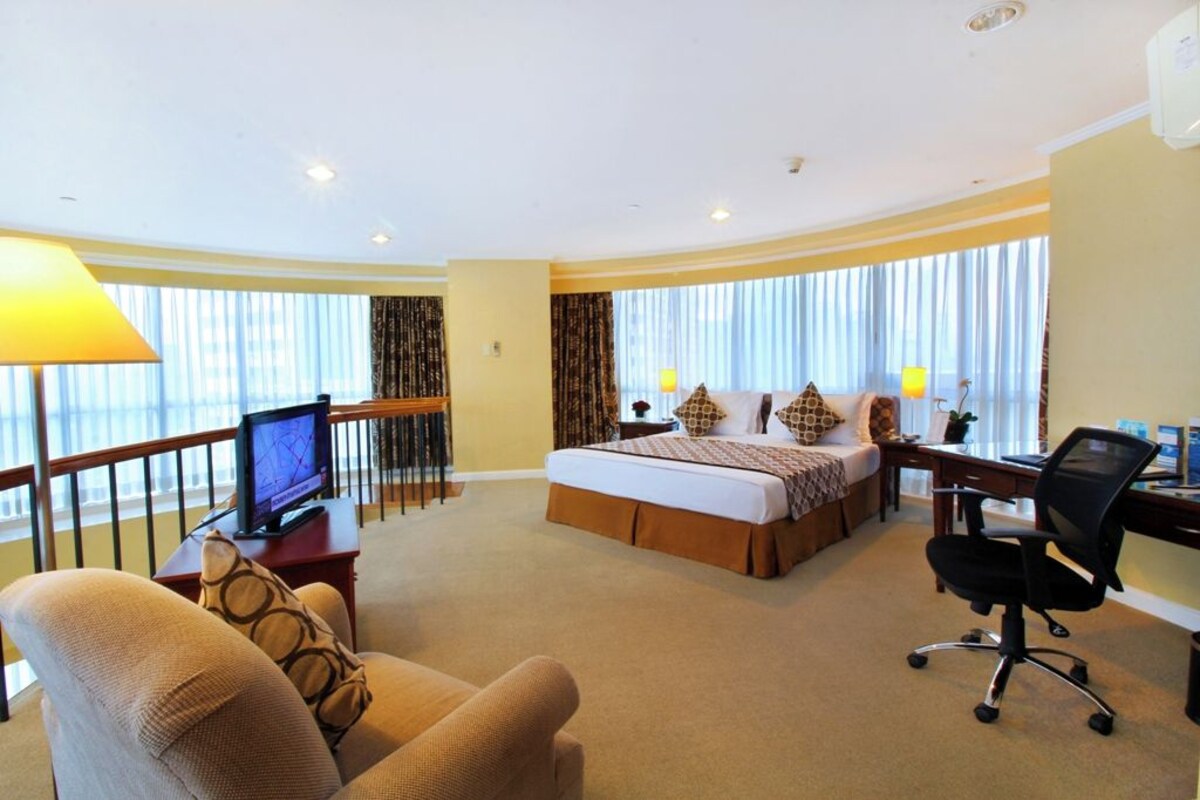 Ein Hotelzimmer mit Bett, Schreibtisch, Stuhl, Fernseher und großen Fenstern.