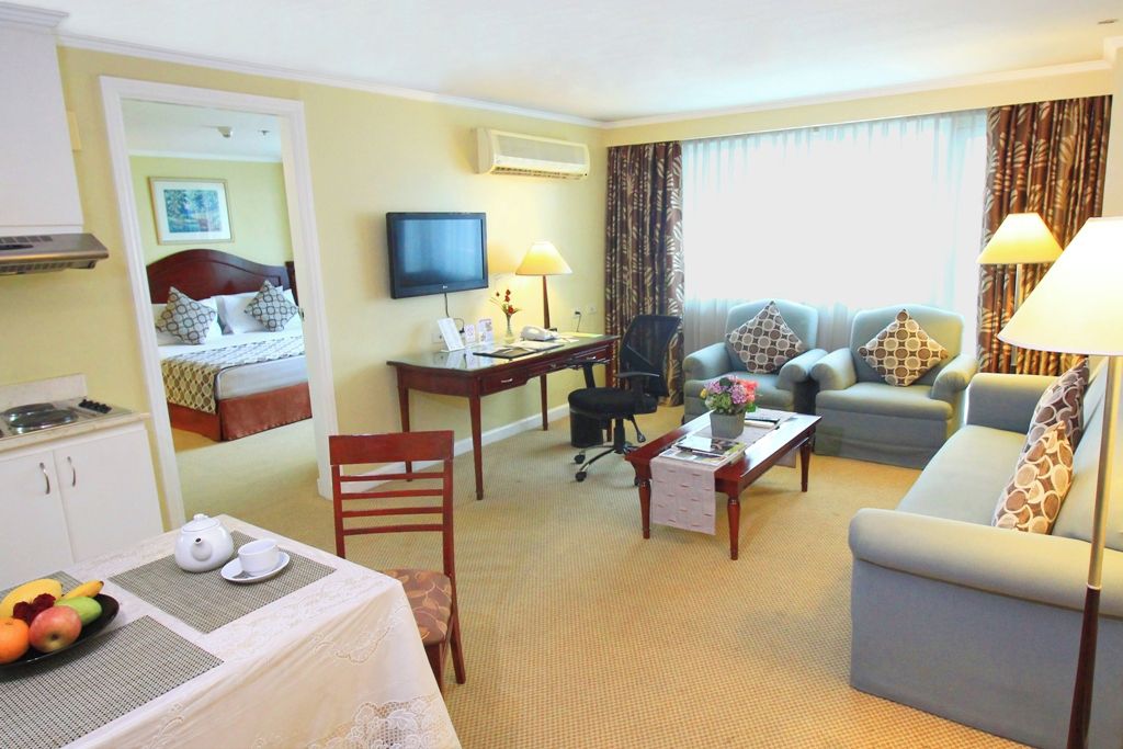 Habitación de hotel con cama, escritorio, televisor, sofá y zona de comedor con mesa para dos.