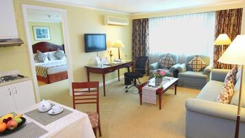 Habitación de hotel con cama, escritorio, televisor, sofá y zona de comedor con mesa para dos.