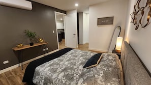 A bedroom with a bed, bedside table, lamp, and a view into the kitchen. - New Listing (Tijuana)