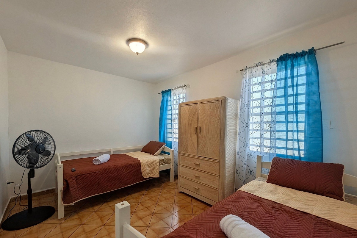 A room with two beds, a wardrobe, a fan, and a window with curtains.