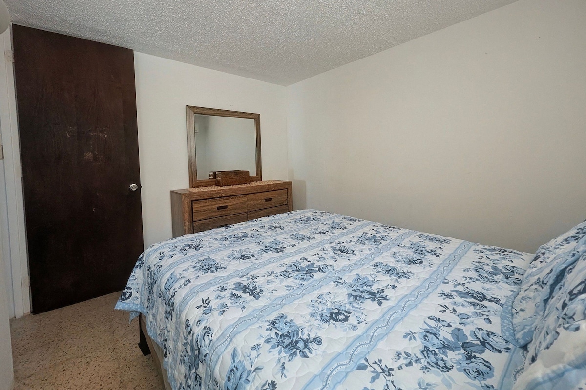 A bedroom with a wooden dresser, a mirror, and a bed with a floral bedspread.