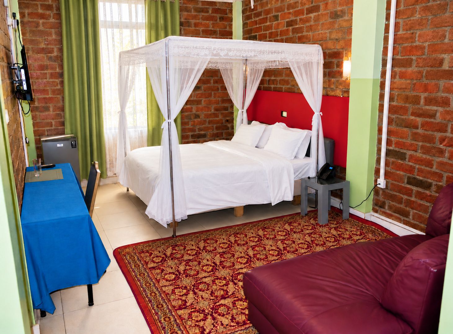 Una habitación con una cama con dosel, un escritorio pequeño con una silla, un teléfono y un sofá rojo.