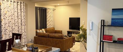 A modern living room with a brown leather sofa, a TV, and a bookshelf with books.