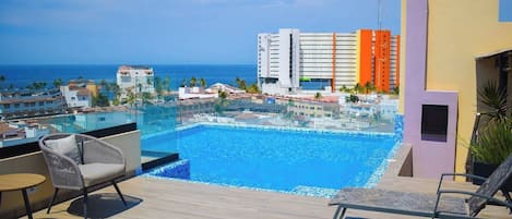 En pool på taket med fri utsikt över havet, omgiven av moderna byggnader och bekväma solstolar.