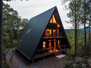 Eine dreieckige Holzhütte mit einem Glasbalkon, umgeben von Bäumen.