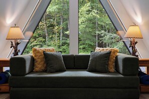 Ein Zimmer mit einem großen Fenster, einem grünen Sofa mit zwei Kissen und je einer Lampe auf beiden Seiten.