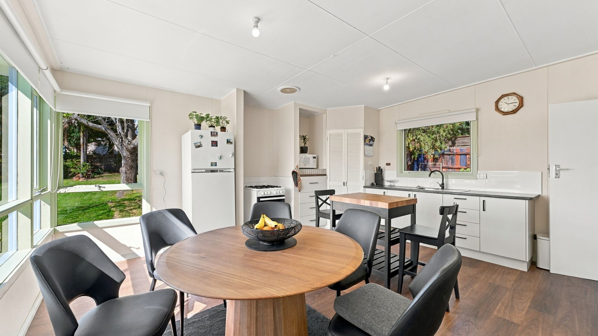 A modern kitchen with a dining area, a refrigerator, a stove, and a window with a view of greenery.