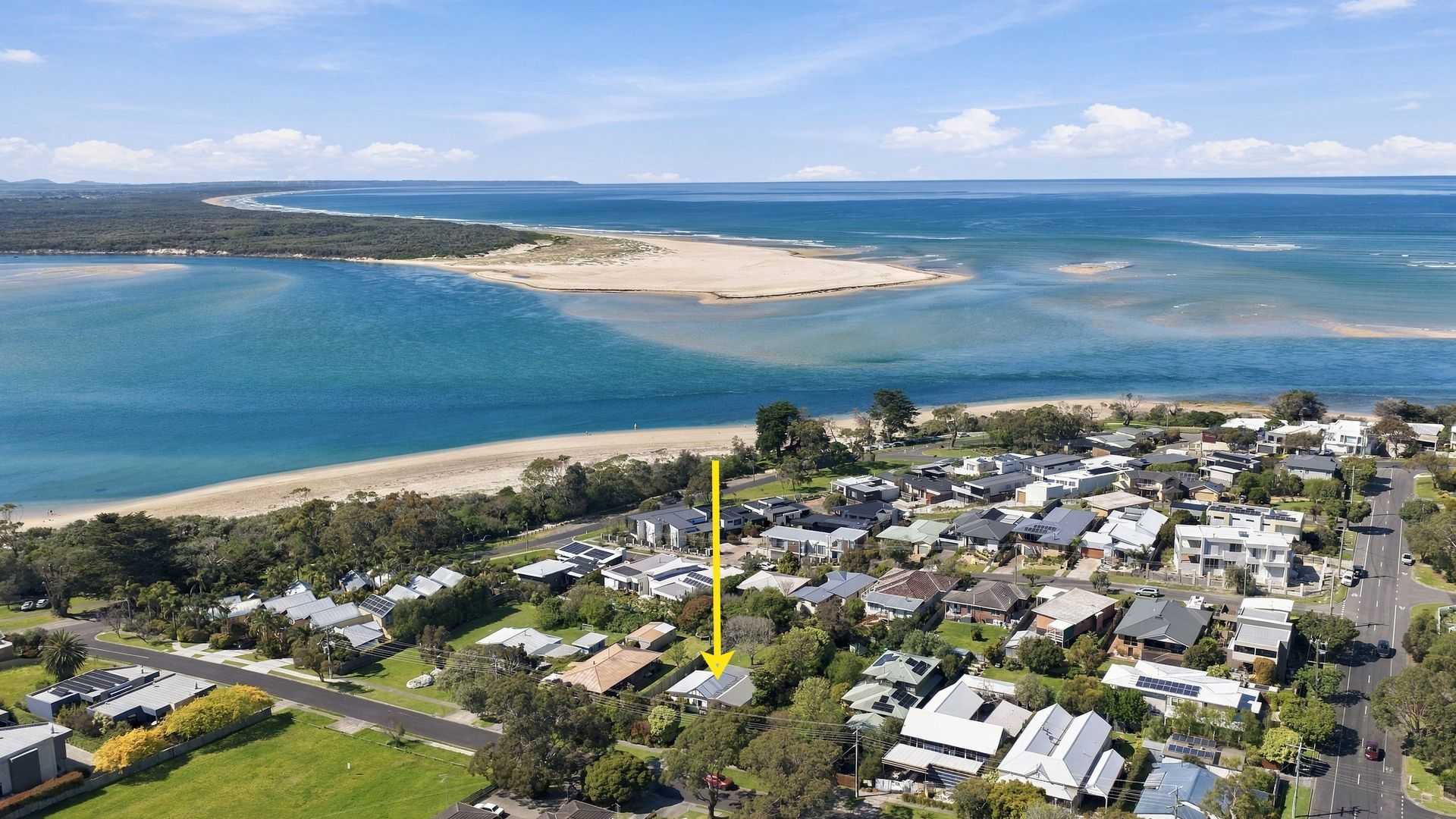 An aerial view of a coastal residential area with houses, a beach, and a large body of water.