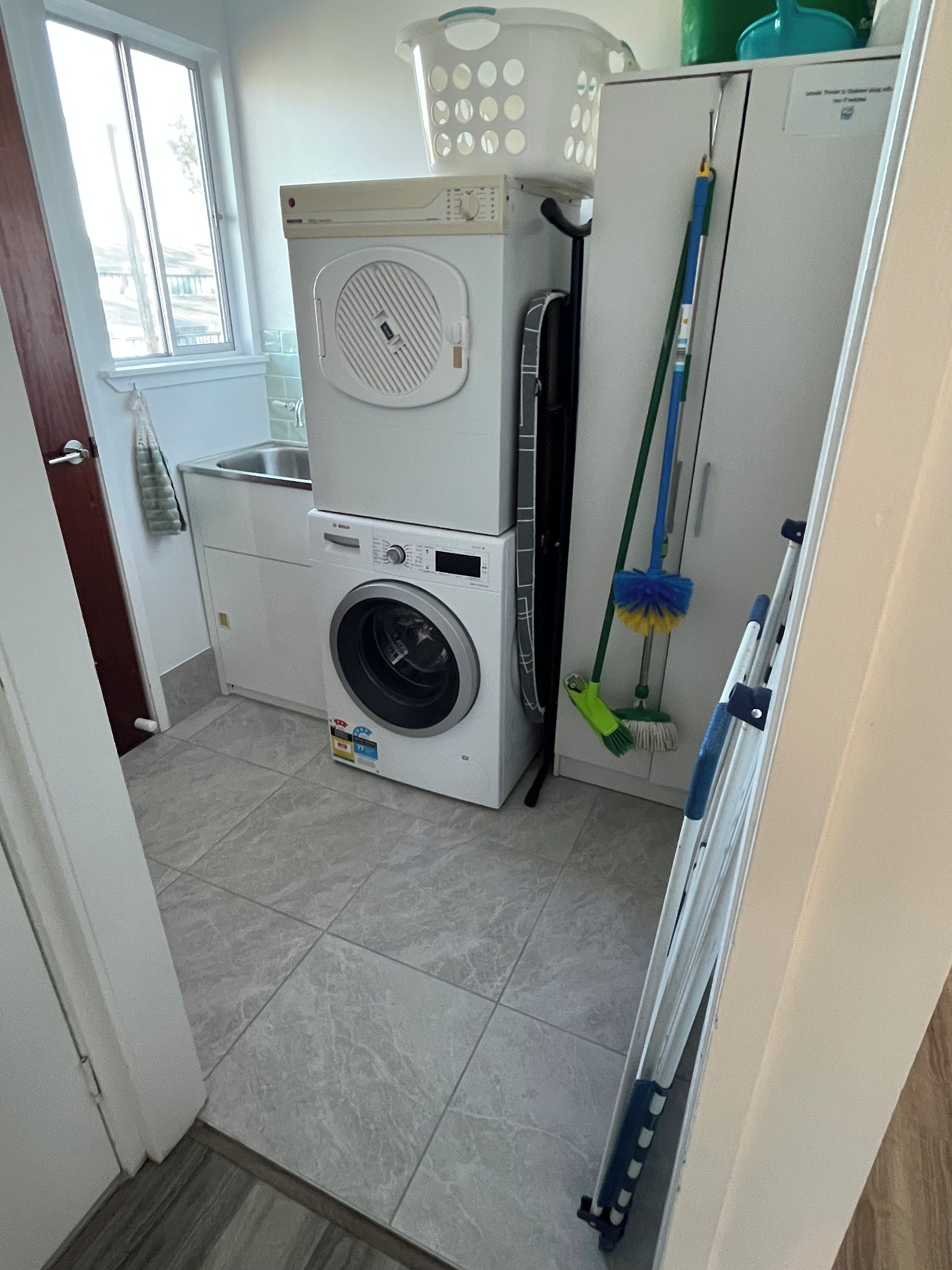 Een wasruimte met een stapel wasmachine en droger, een dweil en een bezem.