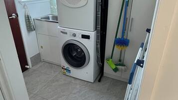 Een wasruimte met een stapel wasmachine en droger, een dweil en een bezem.