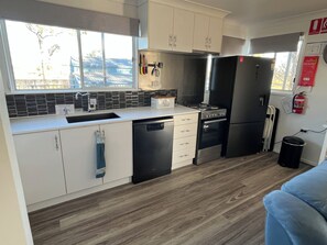 Een kleine keuken met een spoelbak, fornuis, koelkast, en een raam met uitzicht op bomen.
