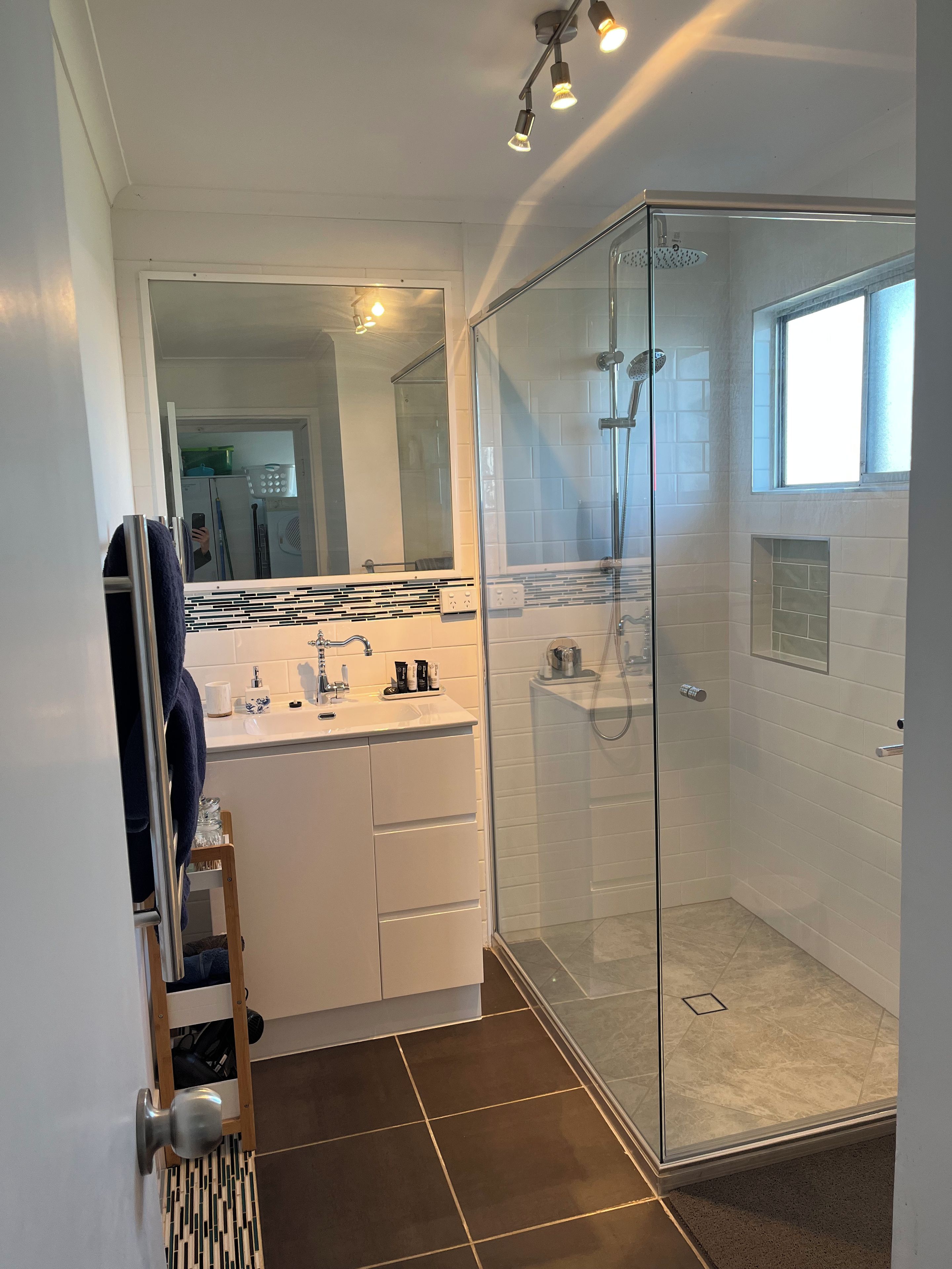 Ein modernes Badezimmer mit einer in Glas abgeschlossenen Dusche, einem weißen Waschtisch mit Spiegel und einem Handtuchhalter.