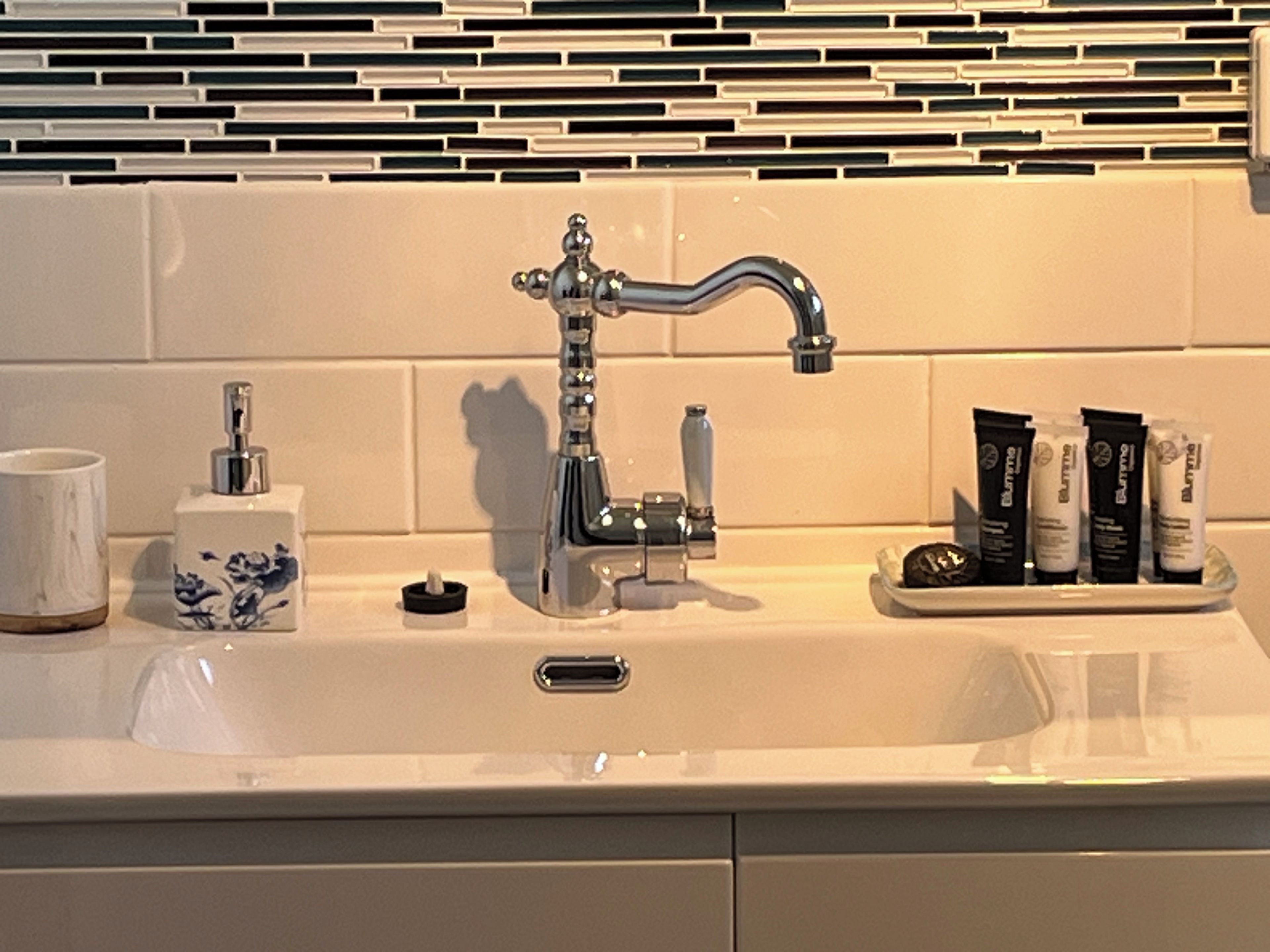 Een badkamermeubel met een wastafel, een moderne kraan, een zeepdispenser en toiletartikelen ernaast.