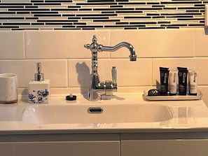 Een badkamermeubel met een wastafel, een moderne kraan, een zeepdispenser en toiletartikelen ernaast.