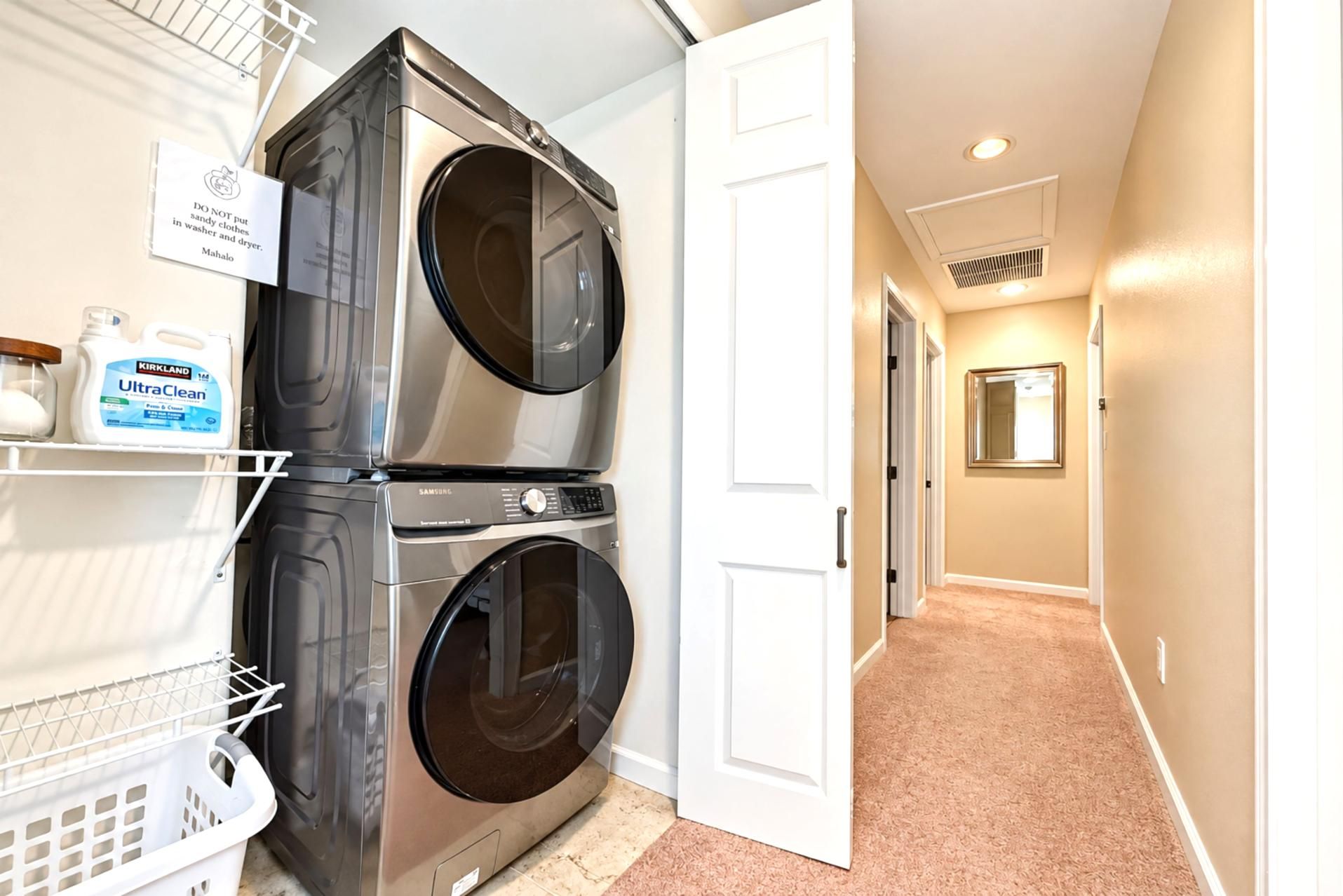 Stacked washer and dryer in a hallway closet, with shelving and a laundry basket for longer stays.
