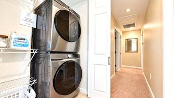 Stacked washer and dryer in a hallway closet, with shelving and a laundry basket for longer stays.